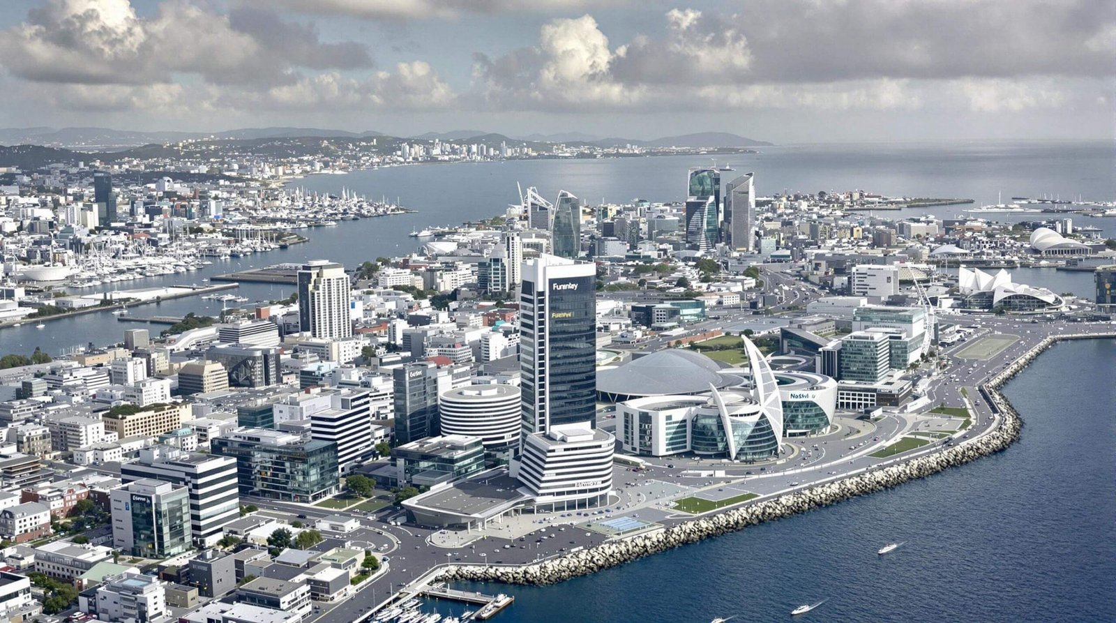 "Aerial view of St. Peter Port financial district in Guernsey with modern office buildings, historic architecture, and harbour area with luxury yachts, under a clear blue sky"