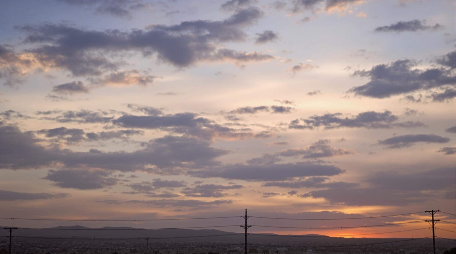 "Tense scene at Lebanon-Israel border checkpoint during sunset, featuring military vehicles, personnel, concrete barriers, barbed wire fencing, and civilians with protest signs, with flags and mountains in the background"