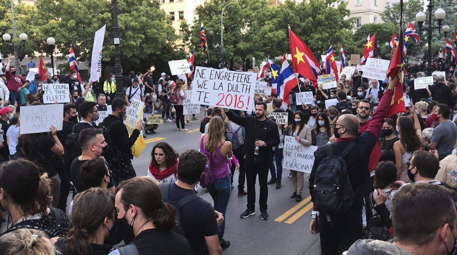 "Large-scale peaceful protest at Syntagma Square, Athens, during sunset showcasing thousands of diverse demonstrators carrying candles, photos of Tempi rail disaster victims, Greek and mourning flags, and signs about rail safety, with Parliament building in the background."