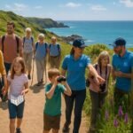 "Diverse group of people exploring a scenic coastal path on Guersney under a sunny sky, with RSPB volunteers showing them local wildlife, amidst fields of wild orchids, rugged cliffs and the sea. Signage about conservation and local wildlife visible in the background."