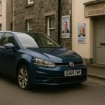 "Parked car with slashed tires on a quiet Guernsey street, campaign posters and local government buildings subtly visible in the background, hinting at political tension following a vandalism incident against a deputy's vehicle in the small island community."